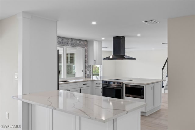 kitchen with kitchen peninsula, wall chimney range hood, and white cabinetry