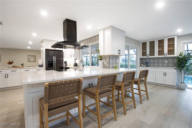 kitchen with stainless steel fridge, white cabinetry, a kitchen breakfast bar, island exhaust hood, and kitchen peninsula