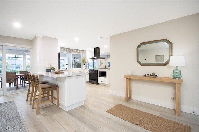 kitchen featuring ventilation hood, white cabinetry, a kitchen breakfast bar, light hardwood / wood-style floors, and kitchen peninsula