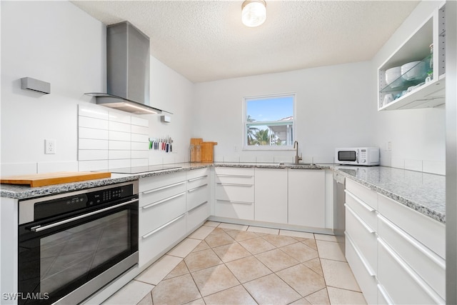 kitchen with a textured ceiling, sink, wall chimney range hood, white cabinets, and oven