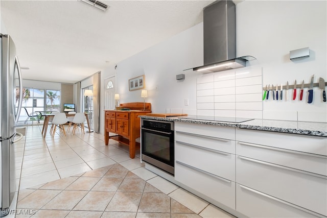 kitchen with light stone counters, wall chimney exhaust hood, stainless steel appliances, light tile patterned floors, and white cabinets