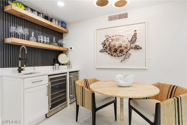 bar featuring wine cooler, sink, light hardwood / wood-style floors, and white cabinets