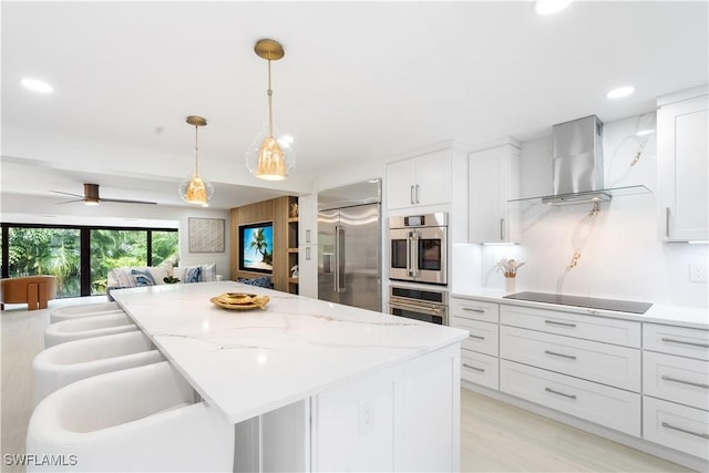 kitchen featuring wall chimney range hood, white cabinets, stainless steel appliances, and hanging light fixtures