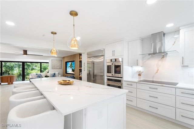 990 8th St S Unit 1B, Naples, FL 34102 - kitchen featuring stainless steel appliances, wall chimney range hood, white cabinetry, pendant lighting, and open floor plan