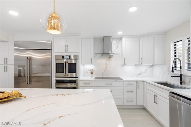 kitchen with sink, hanging light fixtures, wall chimney range hood, stainless steel appliances, and white cabinets