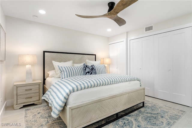 bedroom with two closets, light hardwood / wood-style floors, and ceiling fan