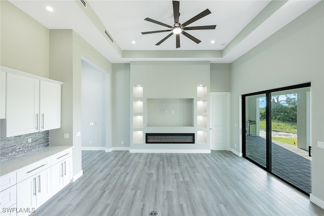 unfurnished living room featuring visible vents, baseboards, light wood-type flooring, a high ceiling, and a glass covered fireplace