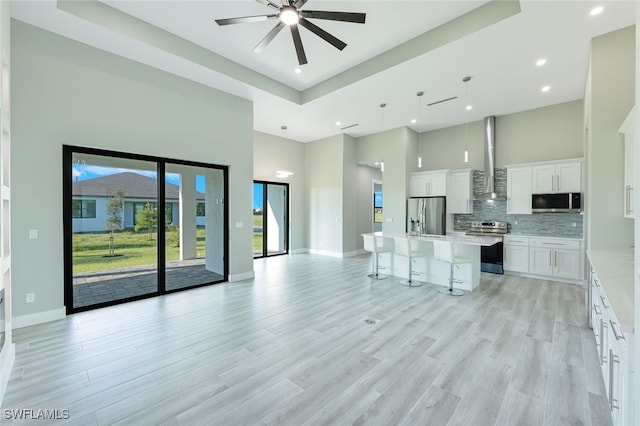 unfurnished living room featuring light wood finished floors, baseboards, ceiling fan, recessed lighting, and a high ceiling