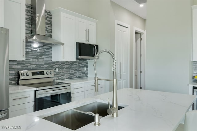 kitchen with light stone counters, decorative backsplash, white cabinets, stainless steel appliances, and wall chimney exhaust hood