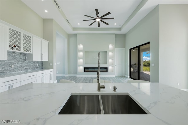 kitchen featuring a sink, a glass covered fireplace, white cabinets, decorative backsplash, and light stone countertops