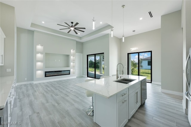 kitchen with light wood-type flooring, a sink, a glass covered fireplace, light stone countertops, and hanging light fixtures