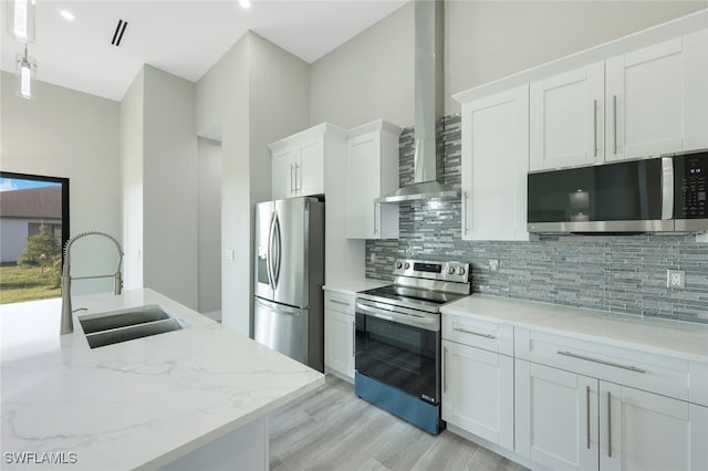 kitchen with tasteful backsplash, stainless steel appliances, white cabinetry, wall chimney exhaust hood, and a sink