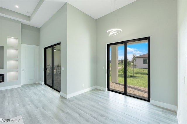 spare room with a towering ceiling, baseboards, and light wood finished floors