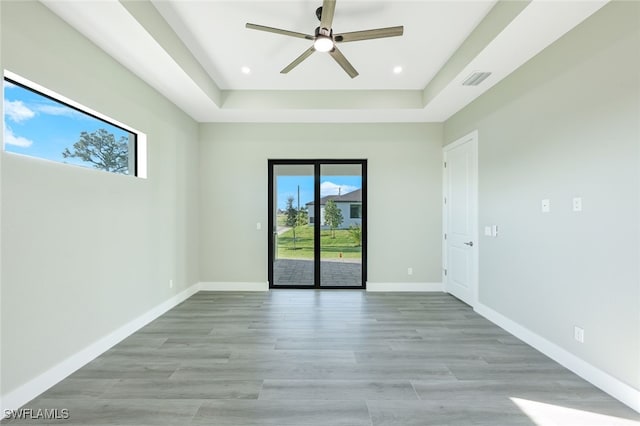 empty room with recessed lighting, light wood-style floors, baseboards, and a raised ceiling