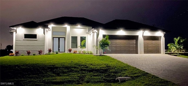 view of front of home with decorative driveway, a lawn, and stucco siding