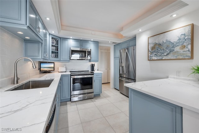 kitchen with a raised ceiling, sink, backsplash, light stone counters, and stainless steel appliances