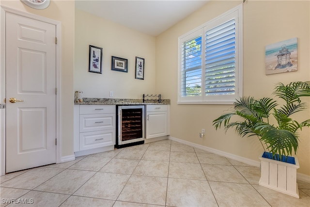 bar with beverage cooler, light stone counters, light tile patterned floors, and white cabinetry