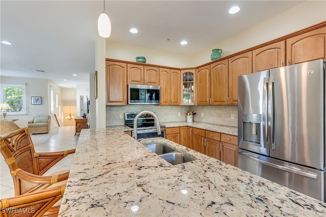 kitchen featuring light stone counters, a breakfast bar, pendant lighting, appliances with stainless steel finishes, and backsplash