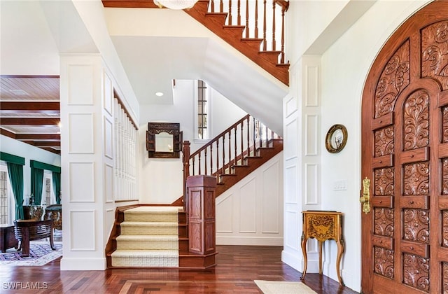 entryway featuring beam ceiling, dark hardwood / wood-style flooring, and a towering ceiling