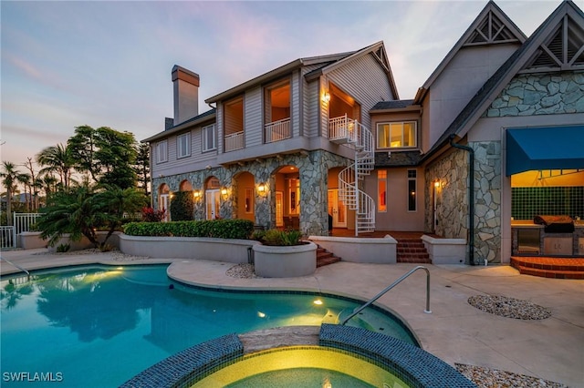 back house at dusk featuring a balcony, a patio, and a pool with hot tub