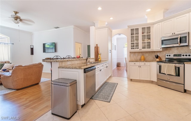 kitchen with stainless steel appliances, light stone countertops, ornamental molding, and white cabinetry