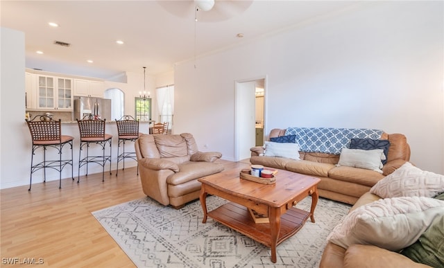 living room with ceiling fan with notable chandelier, crown molding, and light hardwood / wood-style flooring