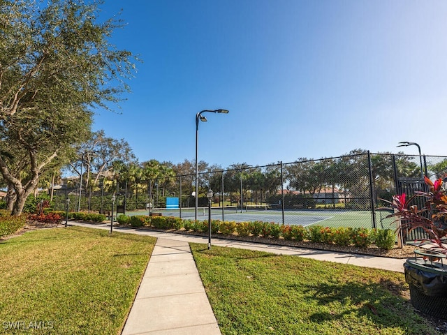 view of tennis court with a lawn and fence