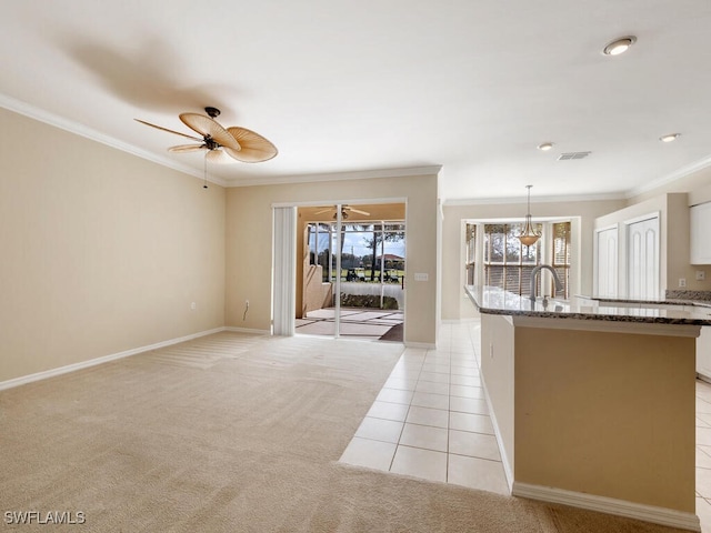 kitchen featuring ceiling fan, light tile patterned flooring, light carpet, dark stone counters, and crown molding