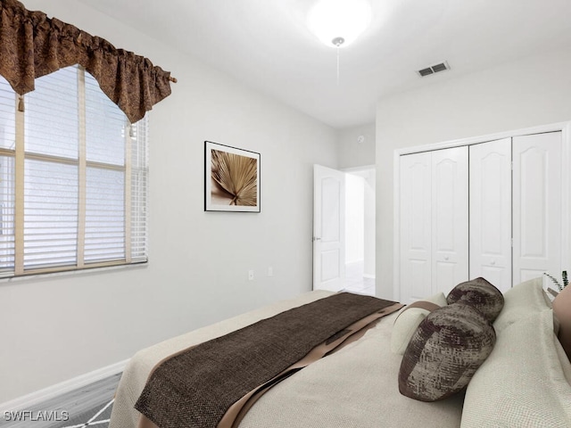 bedroom with a closet, wood finished floors, visible vents, and baseboards