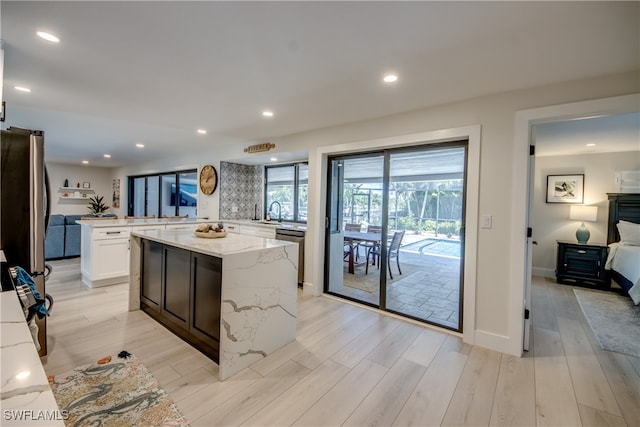 kitchen featuring light stone countertops, stainless steel dishwasher, light hardwood / wood-style floors, kitchen peninsula, and white cabinetry