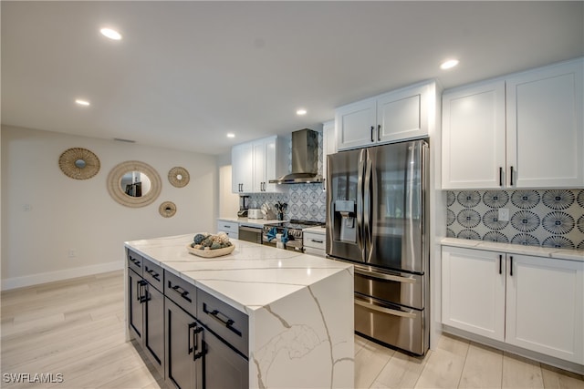 kitchen with light stone counters, stainless steel appliances, tasteful backsplash, wall chimney exhaust hood, and white cabinetry