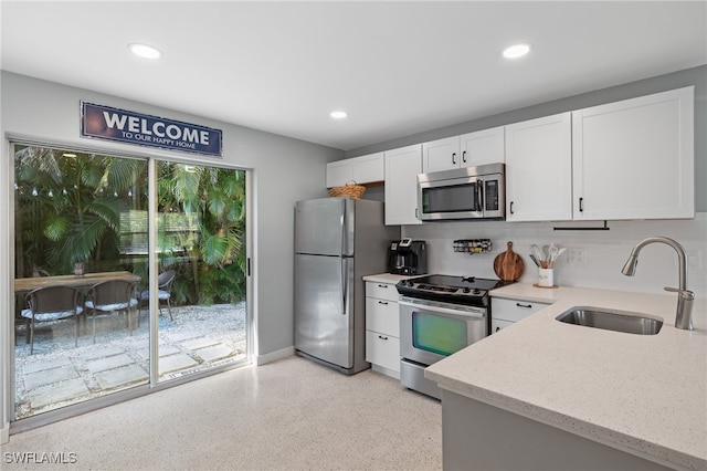 kitchen featuring sink, light stone countertops, backsplash, white cabinets, and appliances with stainless steel finishes