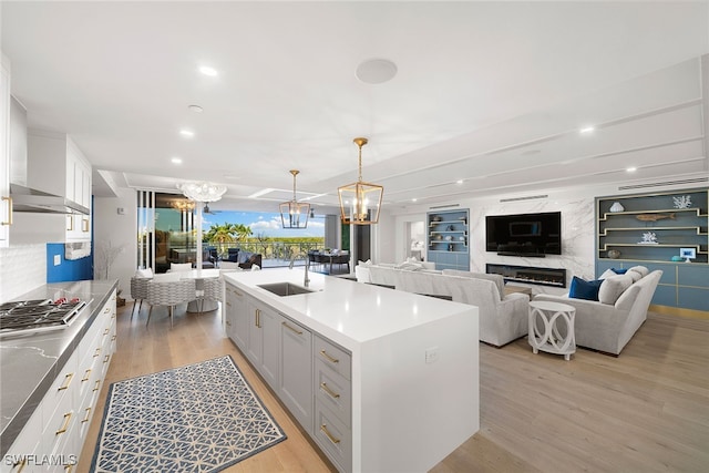 kitchen featuring a kitchen island with sink, pendant lighting, stainless steel gas cooktop, white cabinetry, and light hardwood / wood-style flooring