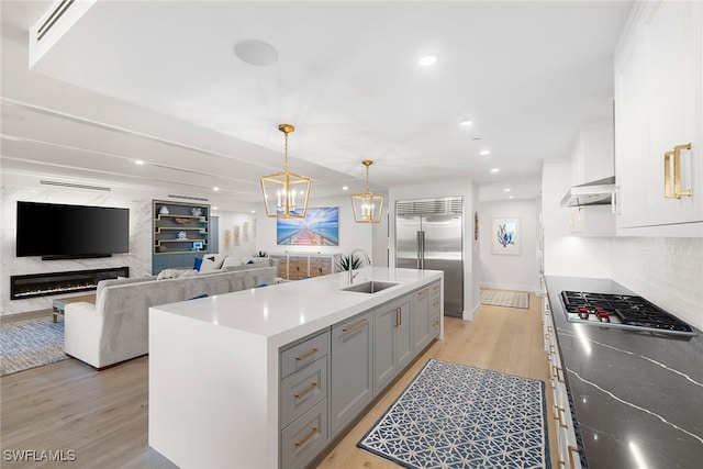 kitchen with appliances with stainless steel finishes, light hardwood / wood-style floors, white cabinets, and a center island with sink