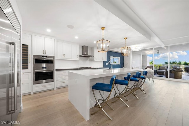 kitchen with wall chimney range hood, a sink, white cabinets, light wood-style floors, and stainless steel appliances