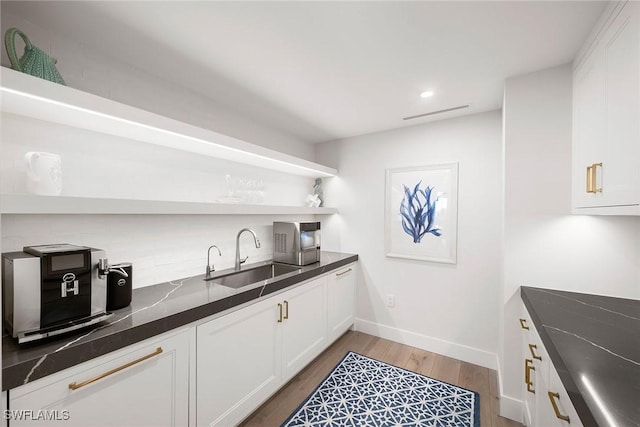 kitchen featuring open shelves, dark countertops, a sink, light wood finished floors, and white cabinetry