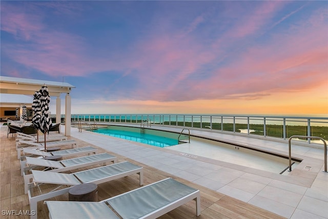 pool at dusk with a water view and a patio area