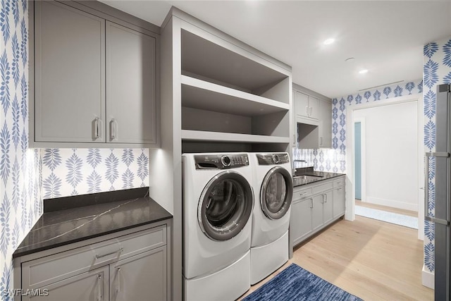 clothes washing area featuring light wood-style floors, wallpapered walls, separate washer and dryer, a sink, and cabinet space