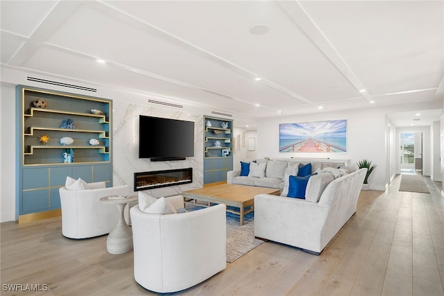 living room with light wood-type flooring, a fireplace, built in shelves, and beamed ceiling