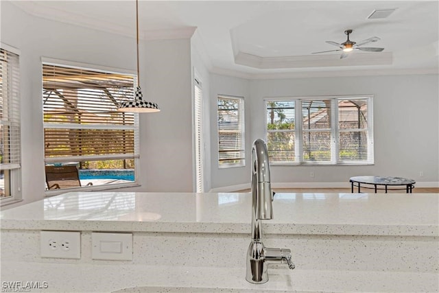 kitchen with ornamental molding, light stone counters, ceiling fan, and a raised ceiling