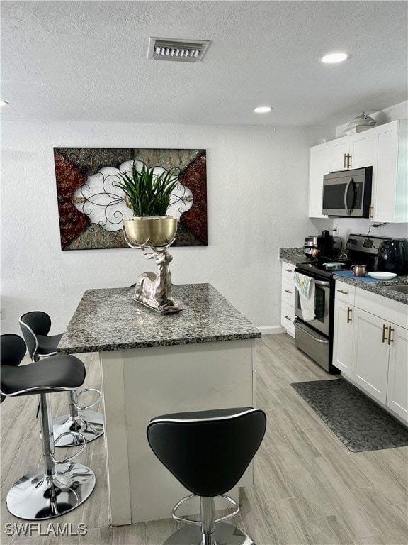 kitchen with dark stone countertops, light hardwood / wood-style flooring, appliances with stainless steel finishes, and white cabinetry