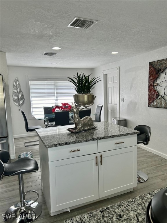 kitchen featuring light stone counters, a textured ceiling, wood-type flooring, and white cabinetry