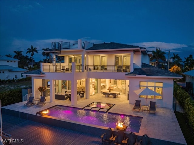 back house at dusk featuring a patio, a balcony, and an outdoor living space with a fire pit