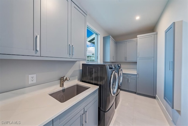 clothes washing area featuring washing machine and dryer, cabinets, light tile patterned floors, and sink