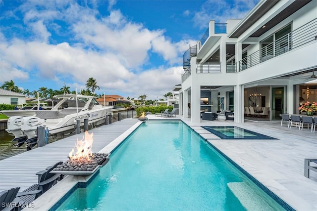 view of pool with a water view, a boat dock, a patio, and an outdoor living space with a fire pit