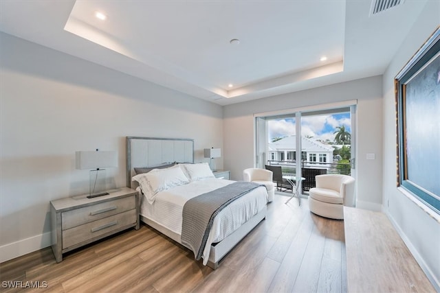 bedroom with access to exterior, a tray ceiling, and wood-type flooring