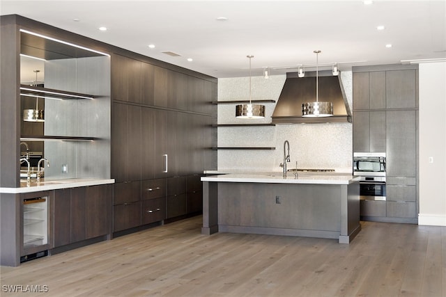 kitchen featuring sink, tasteful backsplash, decorative light fixtures, light hardwood / wood-style flooring, and wall chimney exhaust hood