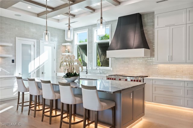 kitchen featuring white cabinetry, light stone counters, light hardwood / wood-style floors, a kitchen island, and custom range hood