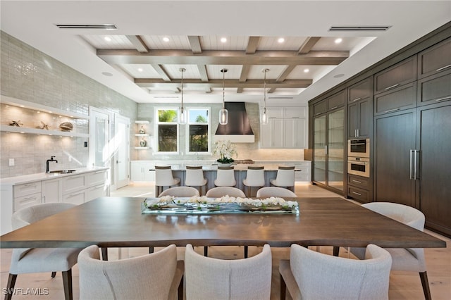 dining room with beam ceiling, light hardwood / wood-style flooring, coffered ceiling, and sink