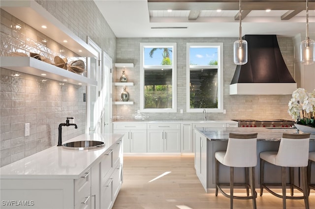 kitchen featuring white cabinetry, a center island, range hood, and sink